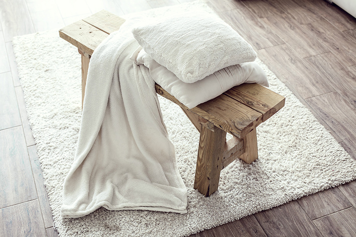 Still life details, stack of white cushions and blanket on rustic bench on white carpet