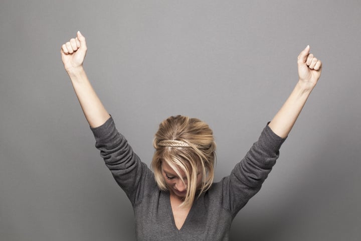 success concept - successful young blonde woman winning a competition with both hands raised up above with head down for thanks and humility