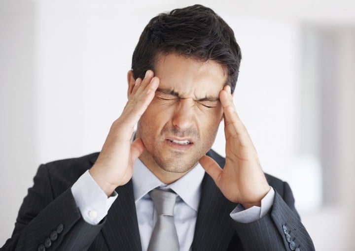 Closeup of young business man with headache rubbing temples